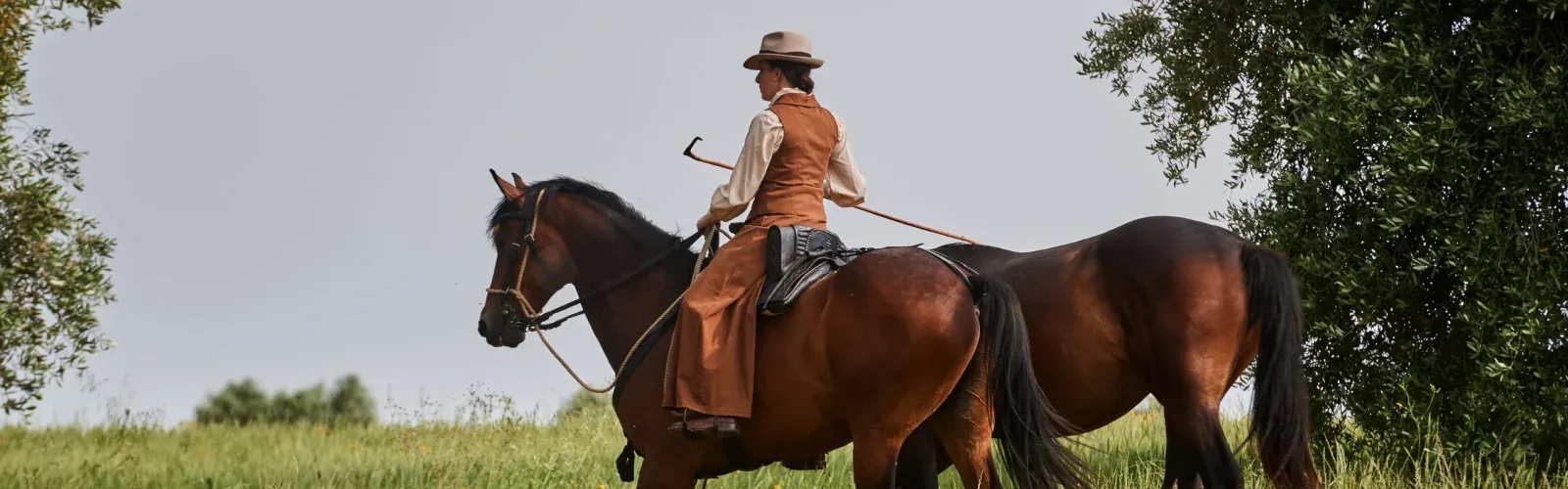 A horse woman riding across the ridges, oak woods, and ancient stone of the territory beyond Agaporia's 70-hectare regenerative estate in Montefollonico, Tuscany