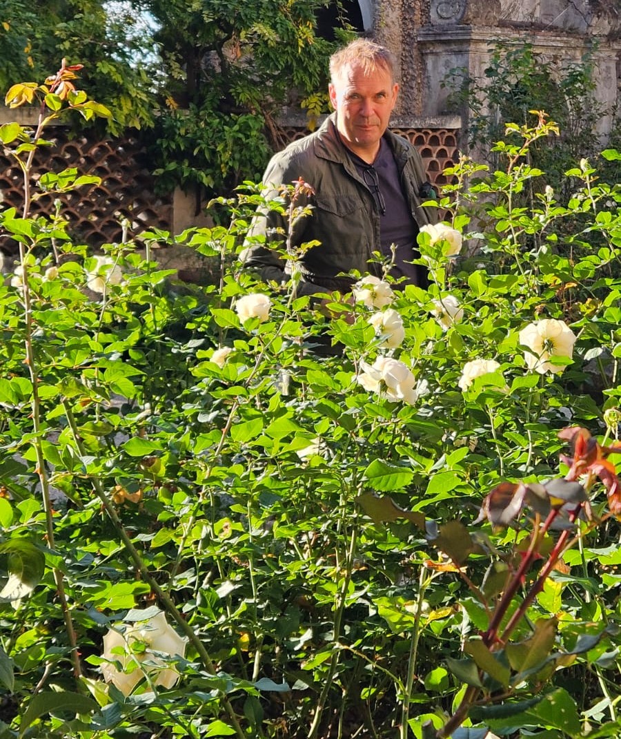 Pascal Steenhuis, Founder of Agaporia, photographed mid-distance among flowering roses in the working garden of the 173-acre estate. Purpose-Driven at the regenerative five-star sanctuary in Tuscany.